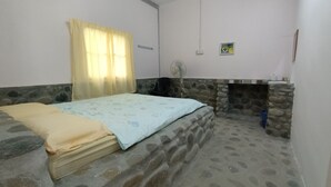 A bedroom with a bed, a stone wall, a small fireplace, a fan, and a window with curtains. - Hotel O Flinstone Lodge (Kota Belud)