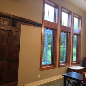 Enjoy a peaceful retreat with a view of the outdoors from this room, featuring a wooden table and chair for dining or working.
