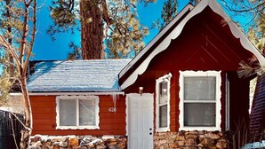 A red house with a stone foundation, a white door, and two windows with shutters.