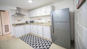 A compact kitchen with white cabinets, a stainless steel refrigerator, a microwave, and a gas stove. - Fully Equipped New 3BR APT->DT->2Mins to the Beach (Sosúa)