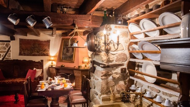 Un'accogliente sala da pranzo in stile rustico con parete in pietra, mensole in legno con stoviglie, un tavolo in legno con sedie e un lampadario dallo stile vintage.