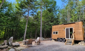 A small wooden cabin with a gravel driveway, surrounded by trees. - Trailside Stays (Rumney)