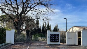Un área de estacionamiento cerrada con un parquímetro digital, un edificio blanco y un árbol grande.