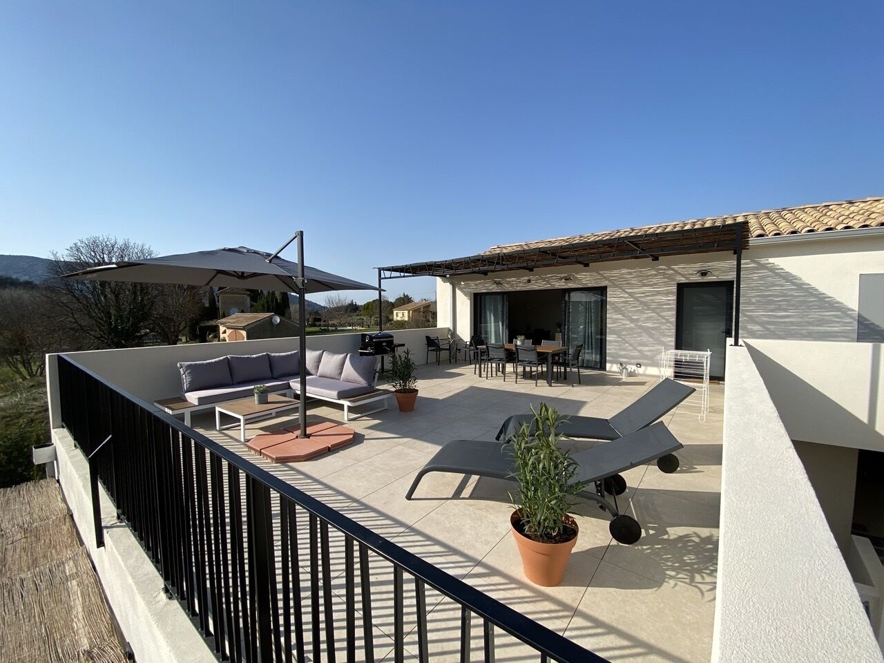 A rooftop terrace with outdoor furniture, a barbecue area, and potted plants.
