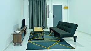 A modern living room with a sofa, a coffee table, a TV on a stand, a small side table, and a door with a curtain. - OYO 90493 JL Homestay (Segamat)