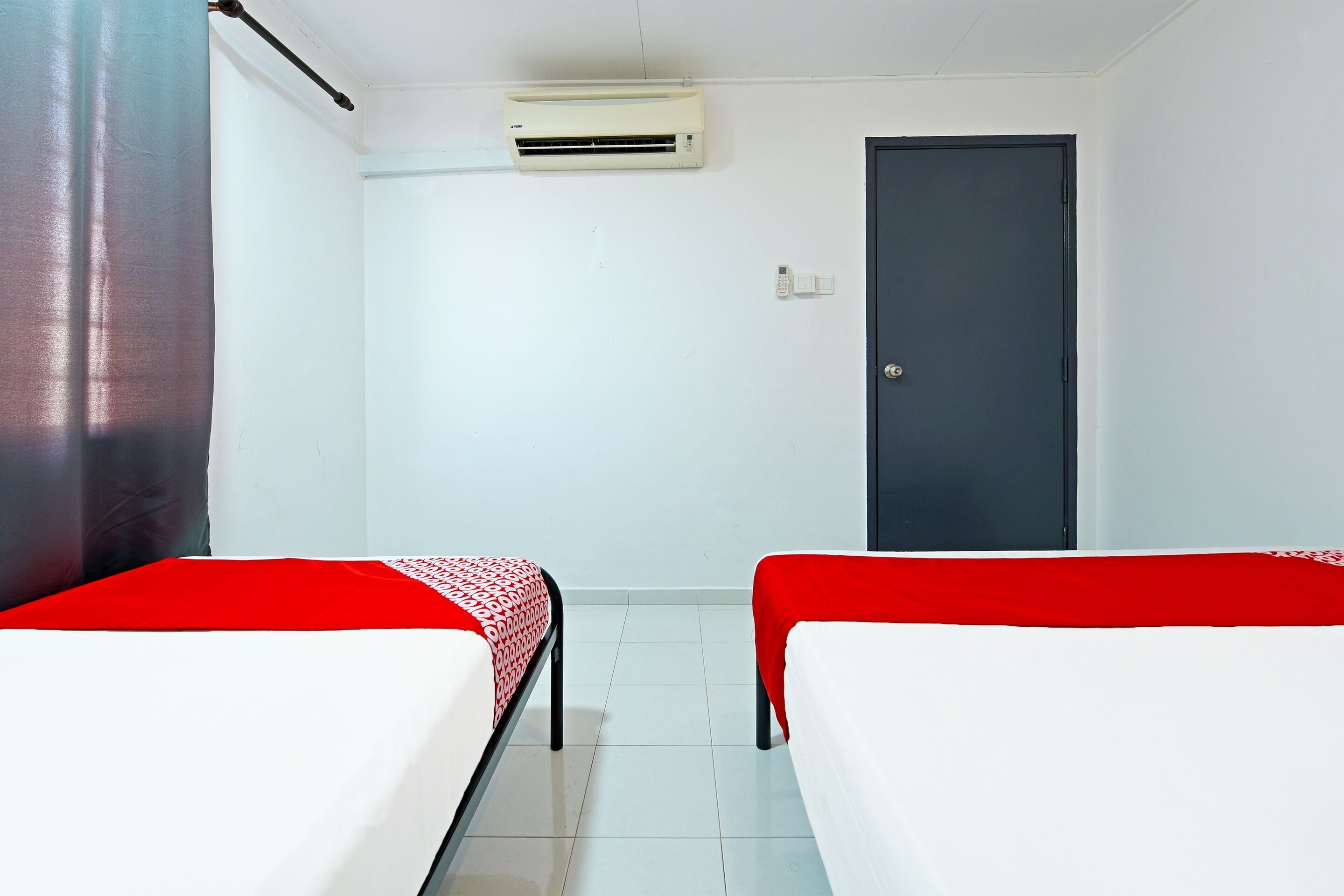 A room with two beds, a door, an air conditioning unit, and a curtain.