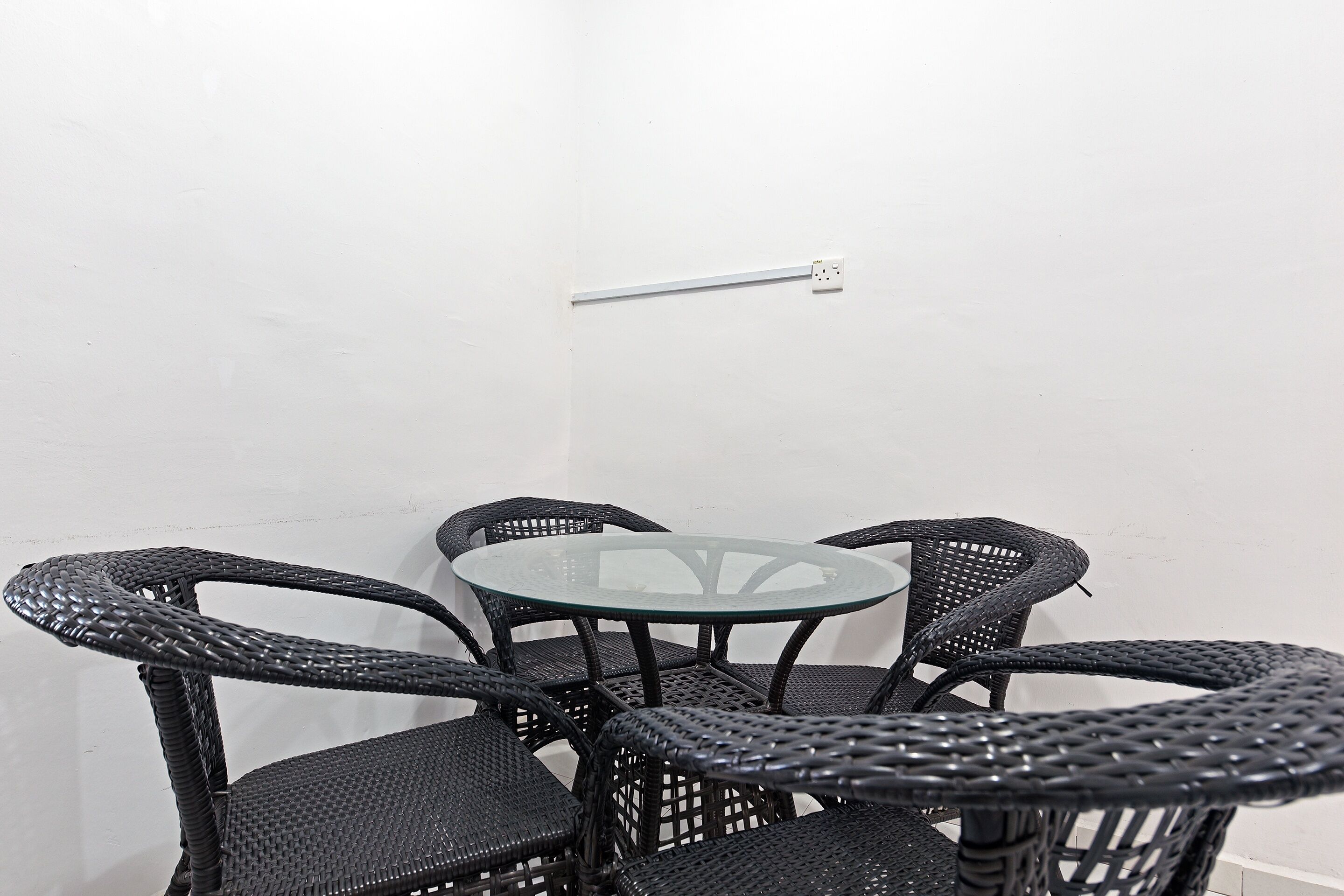Une petite table ronde en verre, accompagnée de quatre chaises en osier noir.