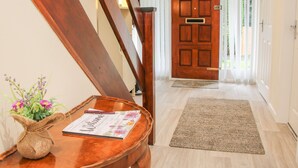 Eine Holztreppe führt zu einer Tür mit einem Brandschutzausgangsschild. Vor der Tür liegt eine Fußmatte und ein gewebter Korb mit Blumen.