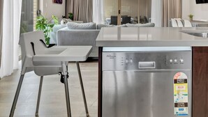 Una cocina moderna con lavavajillas integrado, un comedor con mesa y sillas blancas, y una sala de estar con sofá y cortinas.