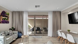 Una sala moderna con sofá, mesa de comedor y sillas. Hay una puerta corredera de vidrio que da a un área exterior con mesa y sillas.
