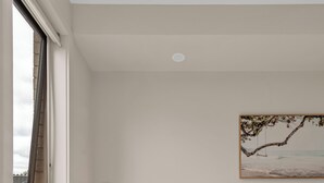 Un dormitorio con cama, mesita de noche, lámpara, planta en maceta y un cuadro en la pared.