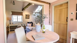 A cozy dining area with a round table, wicker chairs, a book titled "Be My Guest," and a bottle of wine. - The Forge (Stowmarket)
