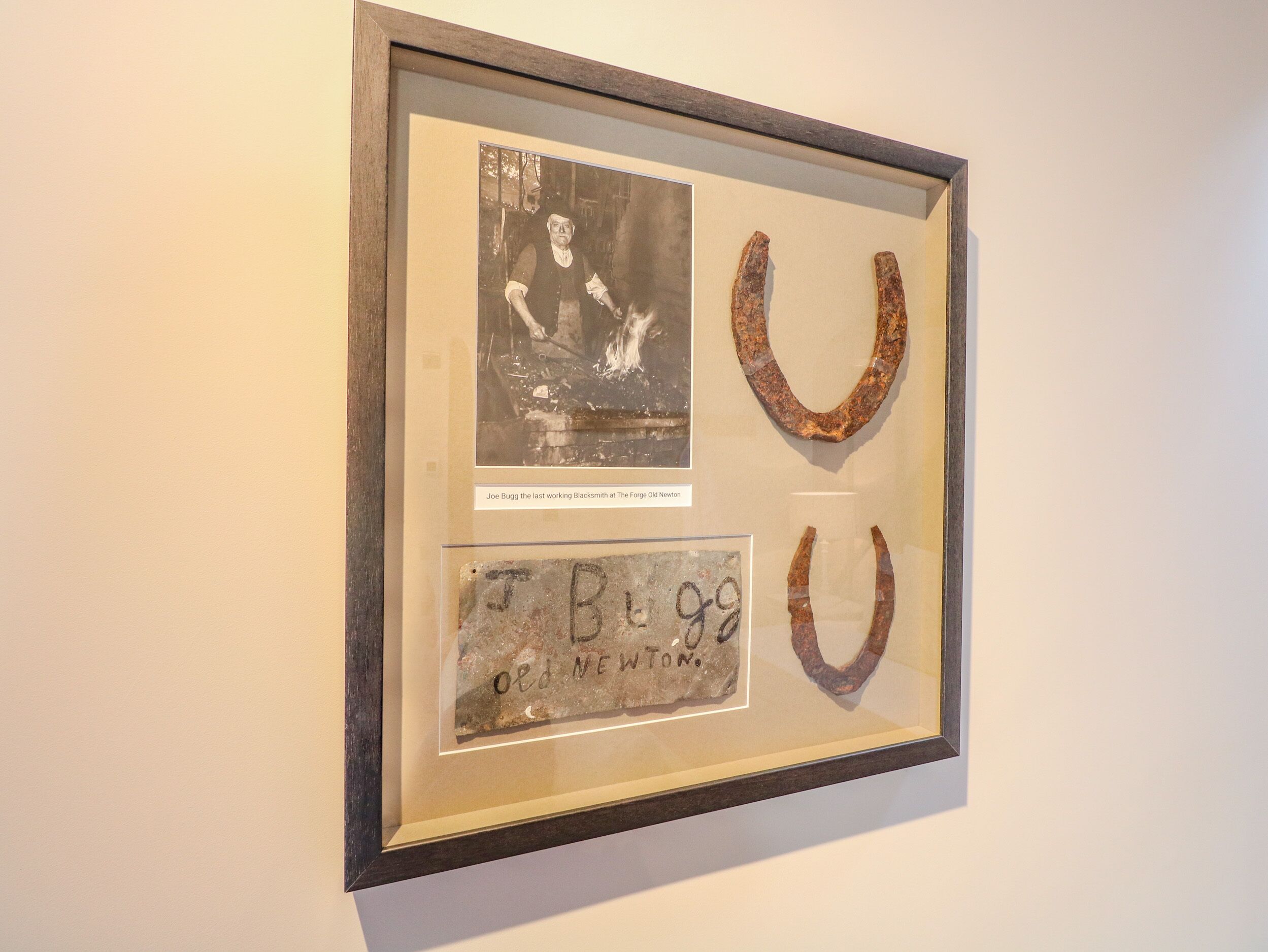 A framed display with a photograph, two horseshoes, and a metal plate with text.