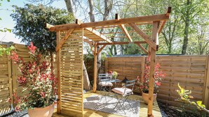A wooden pergola structure with a table and chairs underneath, surrounded by a wooden fence and potted plants. - The Forge (Stowmarket)