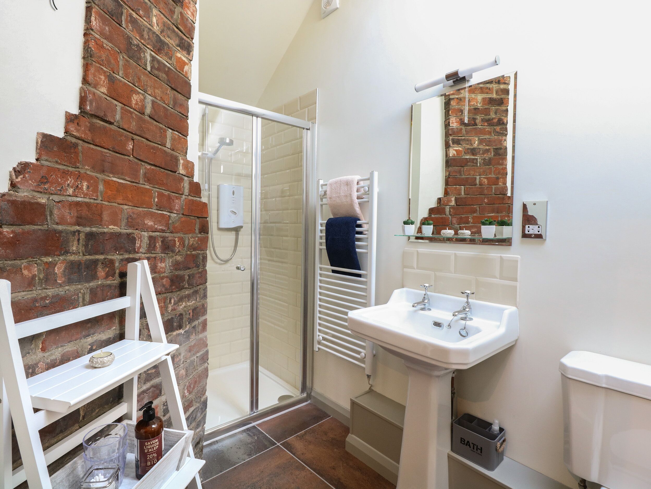 A bathroom with a shower, a sink, a mirror, and a shelf with toiletries.