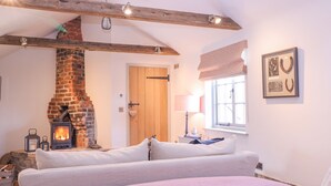 A cozy bedroom with a brick fireplace, a bed with a pink blanket, and a window with a view. - The Forge (Stowmarket)