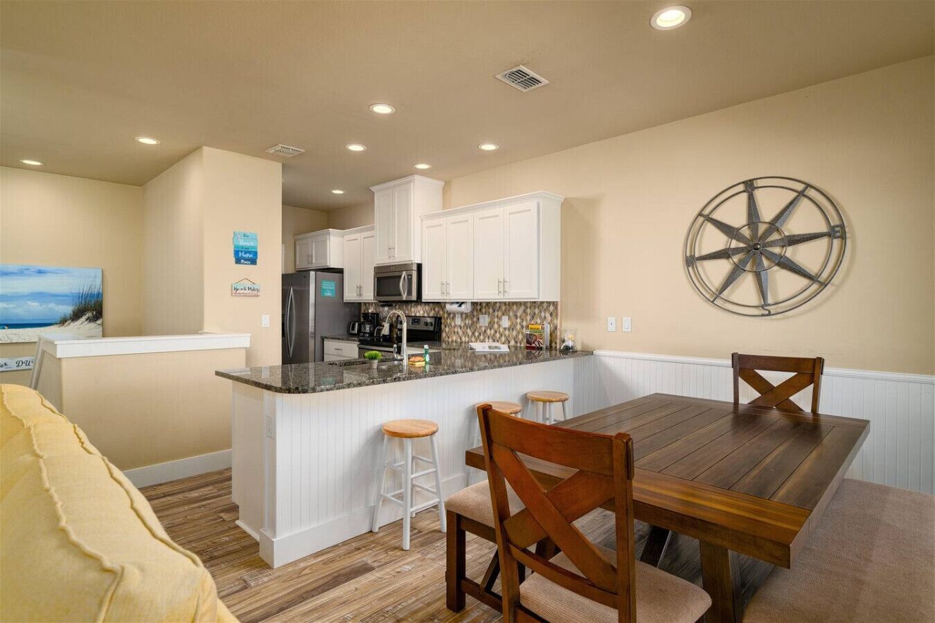 A compact kitchen with white cabinets, a central island with stools, a wooden dining table, and a wall-mounted wheel.