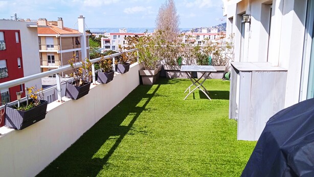 Eine Dachterrasse mit Kunstgrasanlage, Kübelpflanzen und Grillplatz.