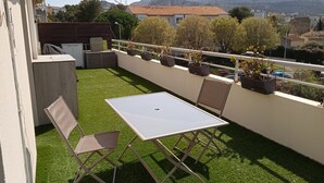 Ein Balkon mit Kunstgrasanlage, einem Tisch, zwei Stühlen und Topfpflanzen.
