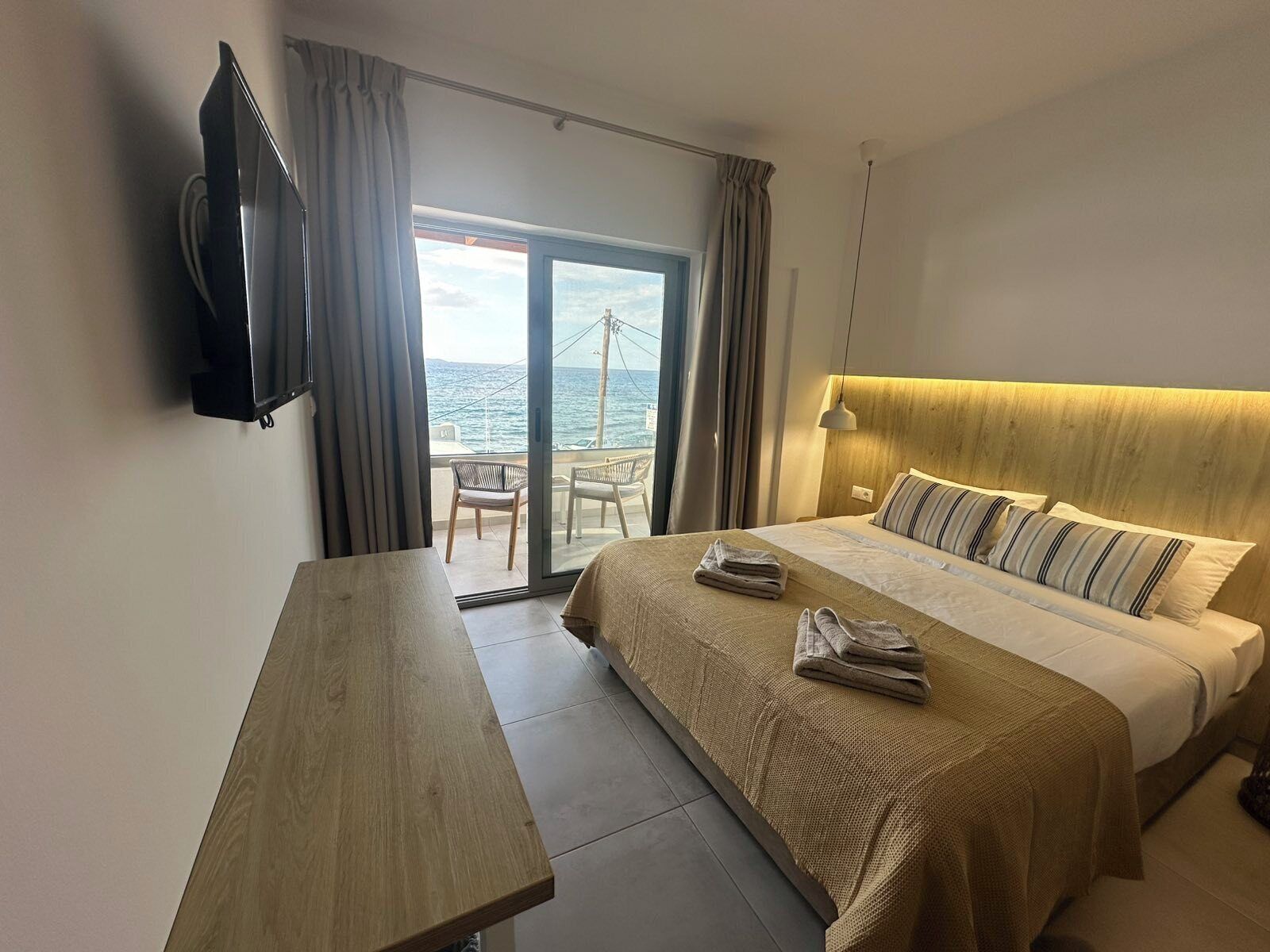 Une chambre d’hôtel avec un lit, une télévision, une table et une vue sur la mer, visible à travers une porte vitrée.