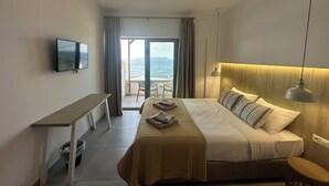 Habitació d'hotel amb llit, escriptori, televisió, finestra amb vista al mar i un balcó.