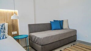 Un dormitori modern amb un sofà llit gris, una petita taula auxiliar blava i una taula de nit blanca.