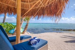 A beachside lounge with a thatched roof, blue cushioned seating, and a view of the ocean.