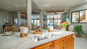 Een ruime keuken met een groot eiland, houten kastjes en uitzicht op de oceaan door grote ramen.