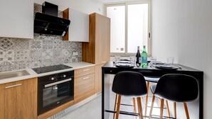 A modern kitchen with wooden cabinets, a black stove, and a dining area with two black chairs. - Perfect Location, Modern 2BR Apartment (Sliema)