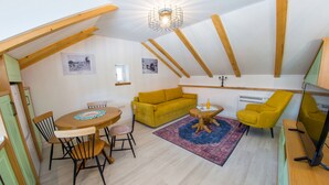Un acogedor loft con techo de madera, un sofá amarillo, una mesa de comedor con sillas y un televisor sobre un mueble de madera.