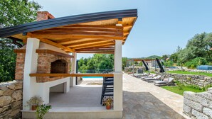 Un espacio al aire libre techado con chimenea de ladrillo, paredes de piedra y sillones de descanso.