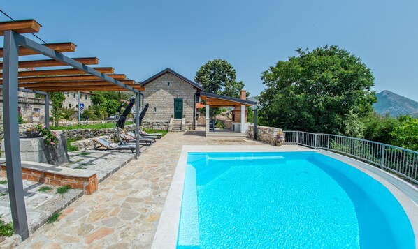 Une piscine avec une terrasse en pierre, un patio couvert et un bâtiment en pierre doté d’une porte verte.