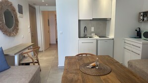 Um espaço de estar compacto com cozinha compacta, uma mesa de jantar com suporte para prato, um sofá e uma cadeira de madeira.