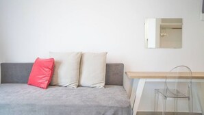 Um sofá cinzento com duas almofadas, uma mesinha de madeira e uma cadeira transparente.