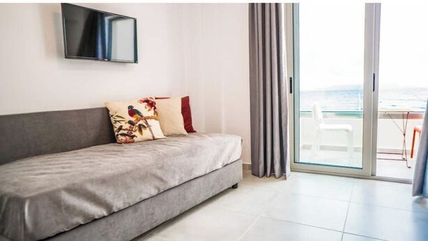 Uma sala de estar moderna com um sofá cinzento, uma televisão de tela plana e uma varanda com vista para o mar.