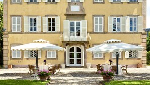 A building with a central entrance, two outdoor seating areas with umbrellas, and a gravel pathway leading to the entrance. - VILLA CONTE - Seven Bedroom Villa, Sleeps 14 (Lucca)