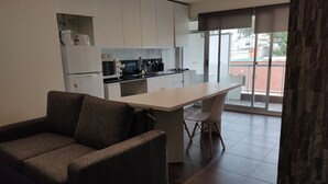 A compact kitchen with white cabinets, a built-in oven, and a dining area with a table and chairs. - Modern, cosy and practical place (Montevideo)