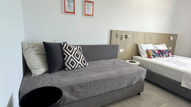 A modern bedroom with a grey sofa, a bed with colorful bedding, and two framed artworks on the wall. - Anfi Suites 3 - Sea View - Sunset Balcony - 3 Guests (Kato Gouves)