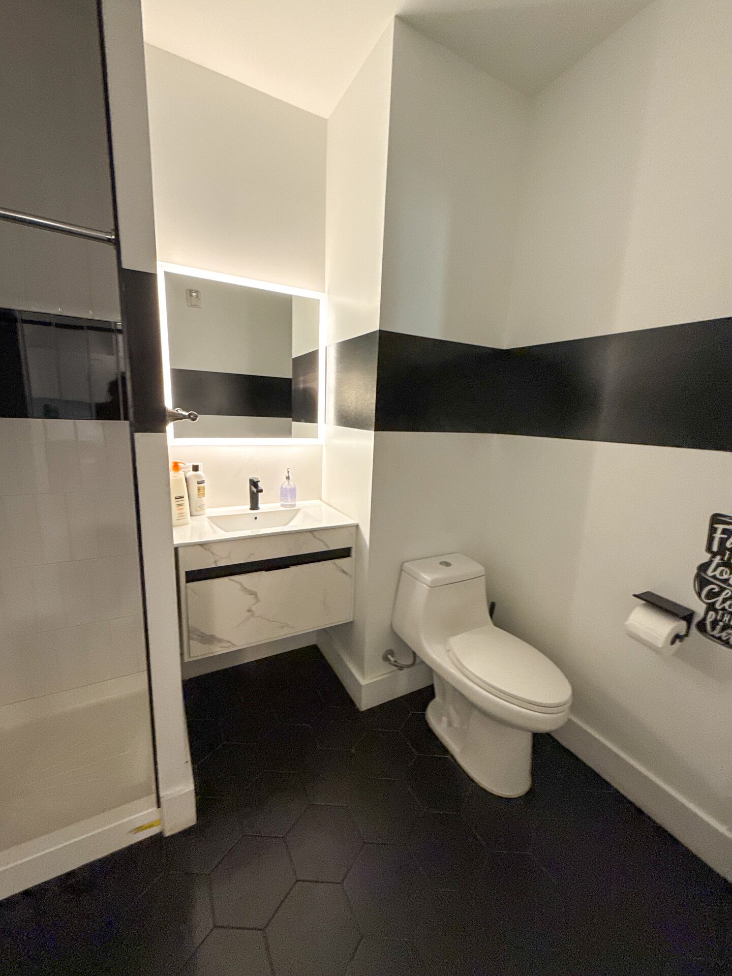 A modern bathroom with a white toilet, a vanity with a mirror, and a black and white striped wall.