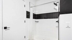 A modern bathroom with a shower, white walls, black hexagonal floor tiles, and a black and white tiled shower area. - Beautiful Studio Near EWR bahz (Elizabeth)