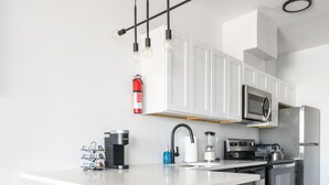 A modern kitchen with white cabinets, stainless steel appliances, a central island with stools, and pendant lighting. - Beautiful Studio Near EWR bahz (Elizabeth)
