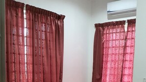 A small room with two beds, red curtains, a white wall, and an air conditioning unit. - OYO Home 90496 Delima Homestay (Alor Setar)