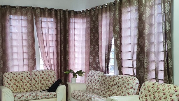 A living room with two white sofas with floral upholstery, a patterned rug, and a potted plant. - OYO Home 90496 Delima Homestay (Alor Setar)