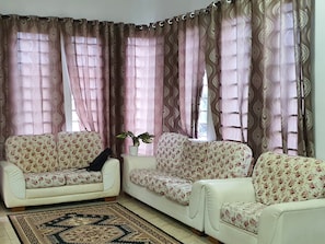 A living room with two white sofas with floral upholstery, a patterned rug, and a potted plant. - OYO Home 90496 Delima Homestay (Alor Setar)