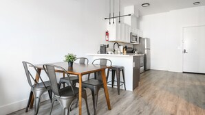 Una cocina moderna con armarios blancos, una isla central y un comedor con sillas de metal y una mesa de madera.