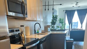 Una cocina moderna con electrodomésticos de acero inoxidable, piso de madera y vistas a la ciudad a través de amplios ventanales.