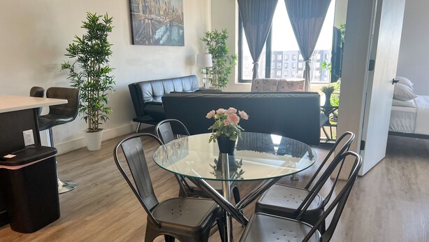 Una sala de estar moderna con una mesa de vidrio para comer rodeada de sillas, un sofá y una planta en maceta.