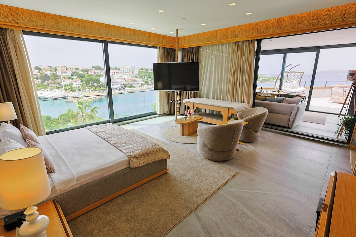 Una habitación de hotel moderna con una cama grande, televisión, sofá y un balcón con vista al mar.