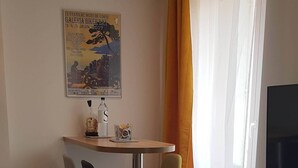 A modern living room with a dining area, featuring a small table, two chairs, a sofa, and a TV mounted on the wall.