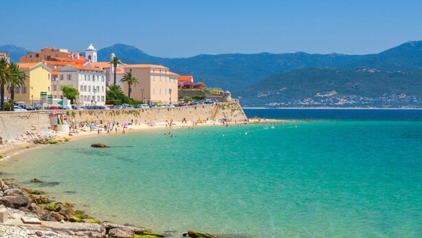 A coastal town with a beach, buildings, and mountains in the background.